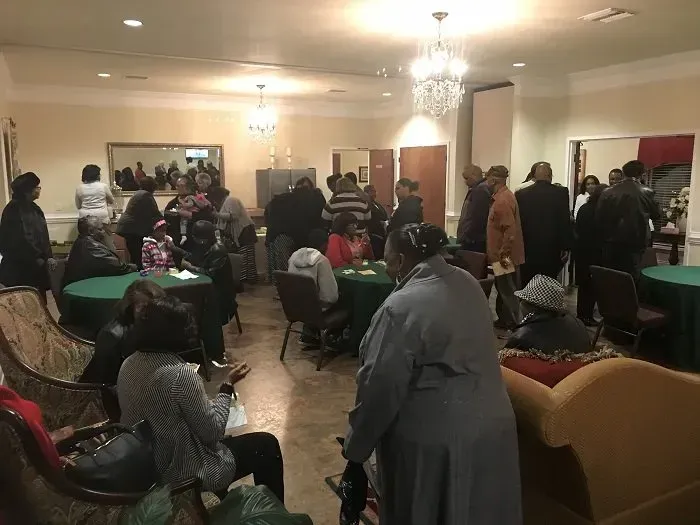 A room filled with people socializing, standing and sitting at round tables covered with dark green tablecloths.