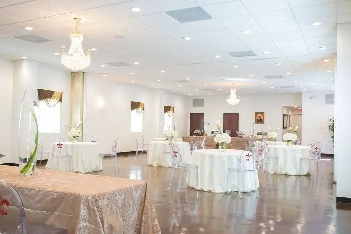 A bright, spacious event hall featuring multiple round tables with white tablecloths and centerpieces under soft lighting.