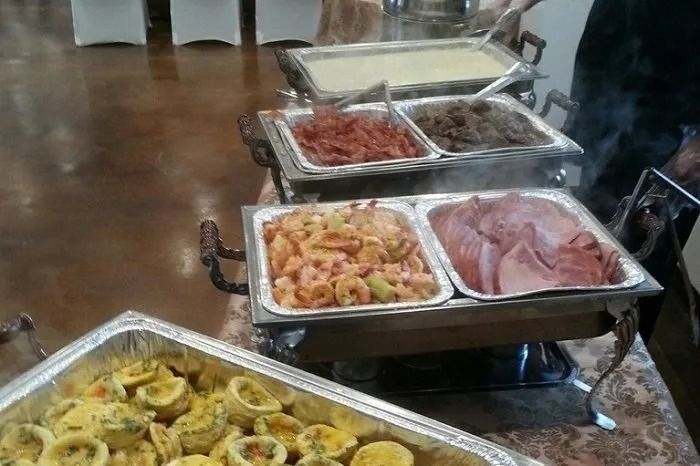 A buffet serving station with multiple chafing dishes containing various cooked foods like shrimp, ham, and vegetables.