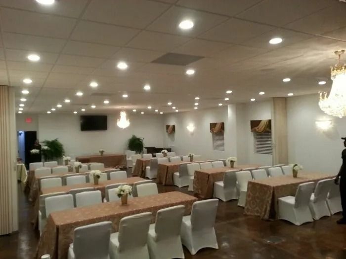 A banquet hall set for a meal with rows of tables covered in gold cloths and white chairs under recessed ceiling lights.