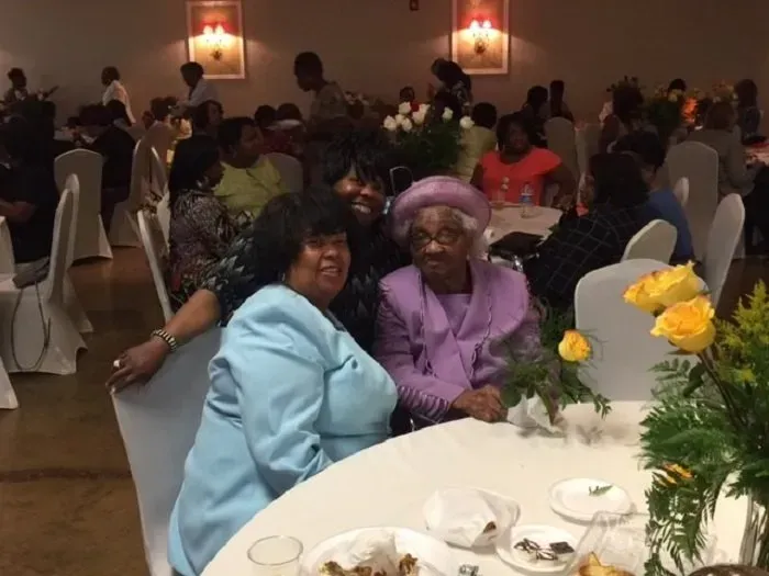 Three people posing for a photo at a banquet table with yellow roses in a decorated event hall.