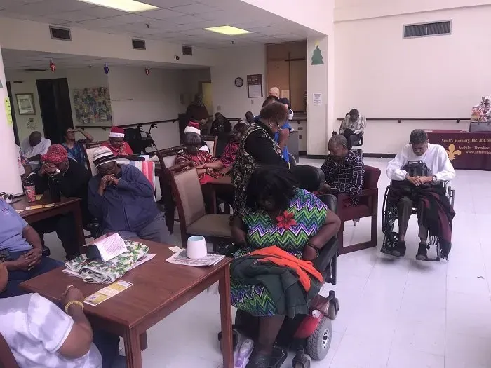 People in a room gathered around tables, some in wheelchairs, with holiday decorations.