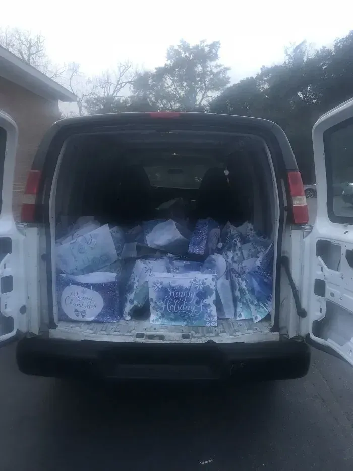 Back view of a white van with open doors filled with boxes wrapped in blue and white decorative paper.