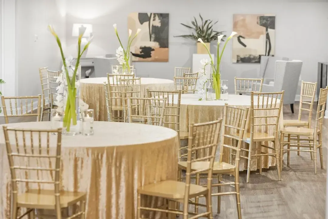 A banquet hall with round tables covered in gold cloths, gold Chiavari chairs, and floral centerpieces.