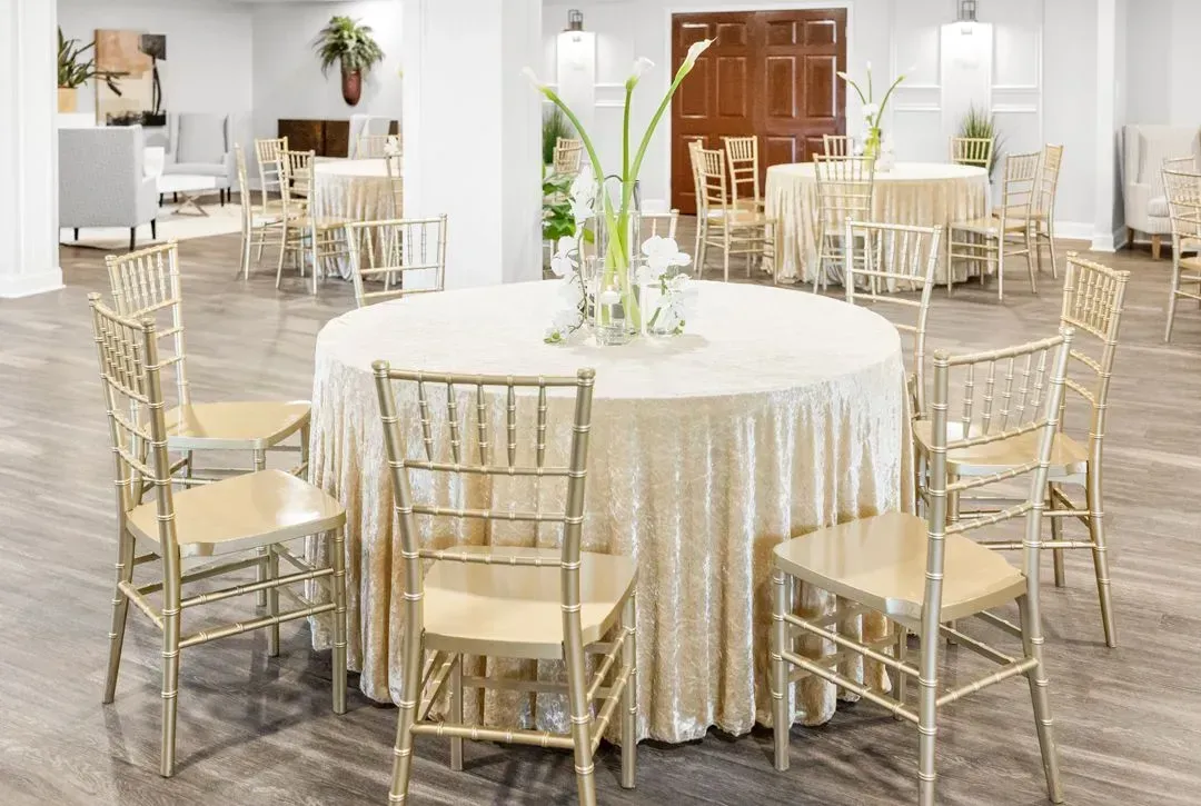 A formal event space with gold Chiavari chairs set around circular tables topped with champagne-colored linens.