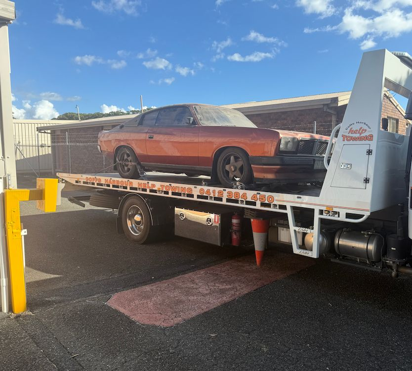 Red Car Loaded on a Tow Truck Flatbed in a Parking Lot Under a Blue Sky — Coffs Harbour Help Towing in Coffs Harbour, NSW