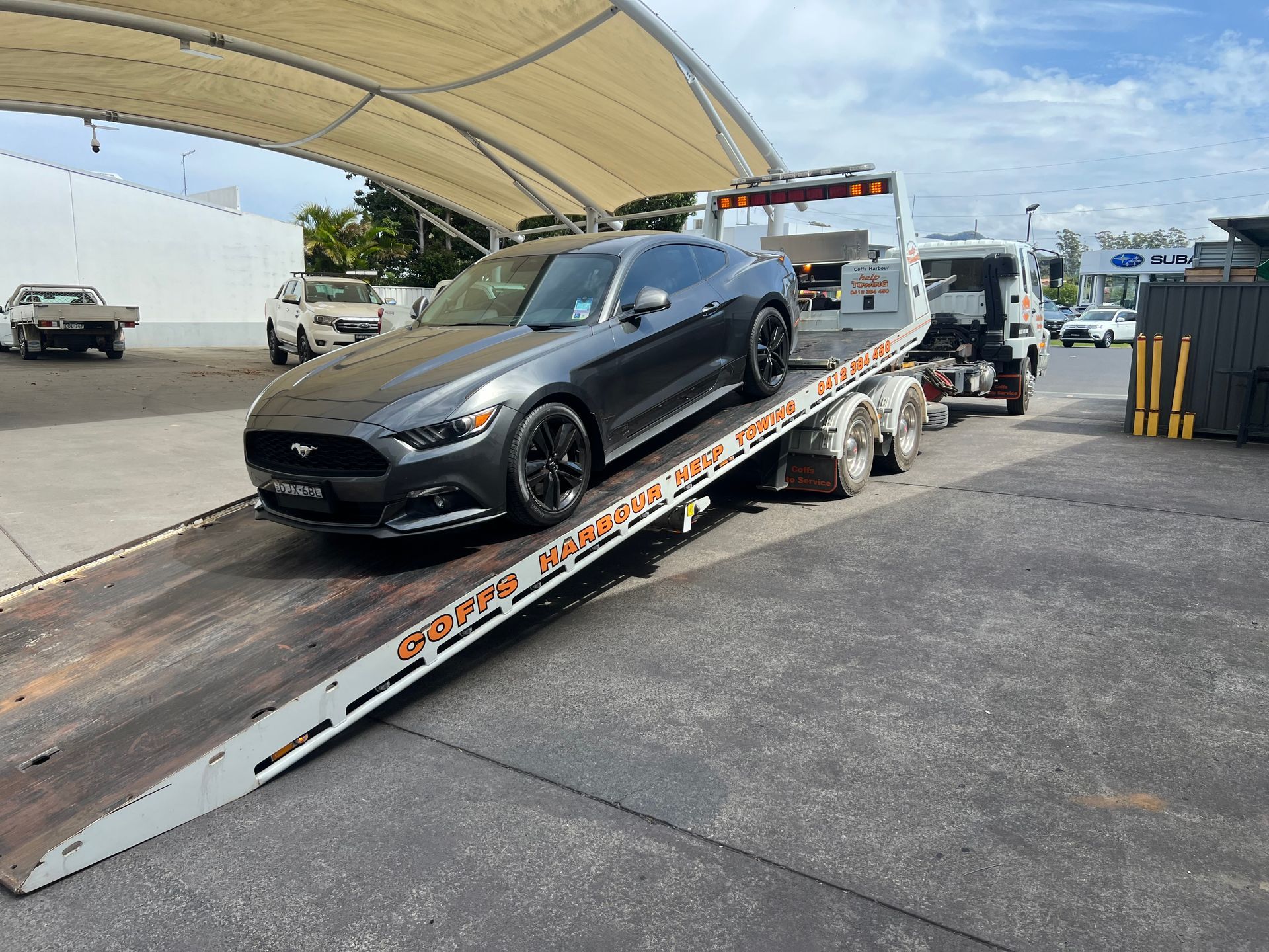 Black sports car being loaded onto a tow truck at an outdoor lot under a canopy.