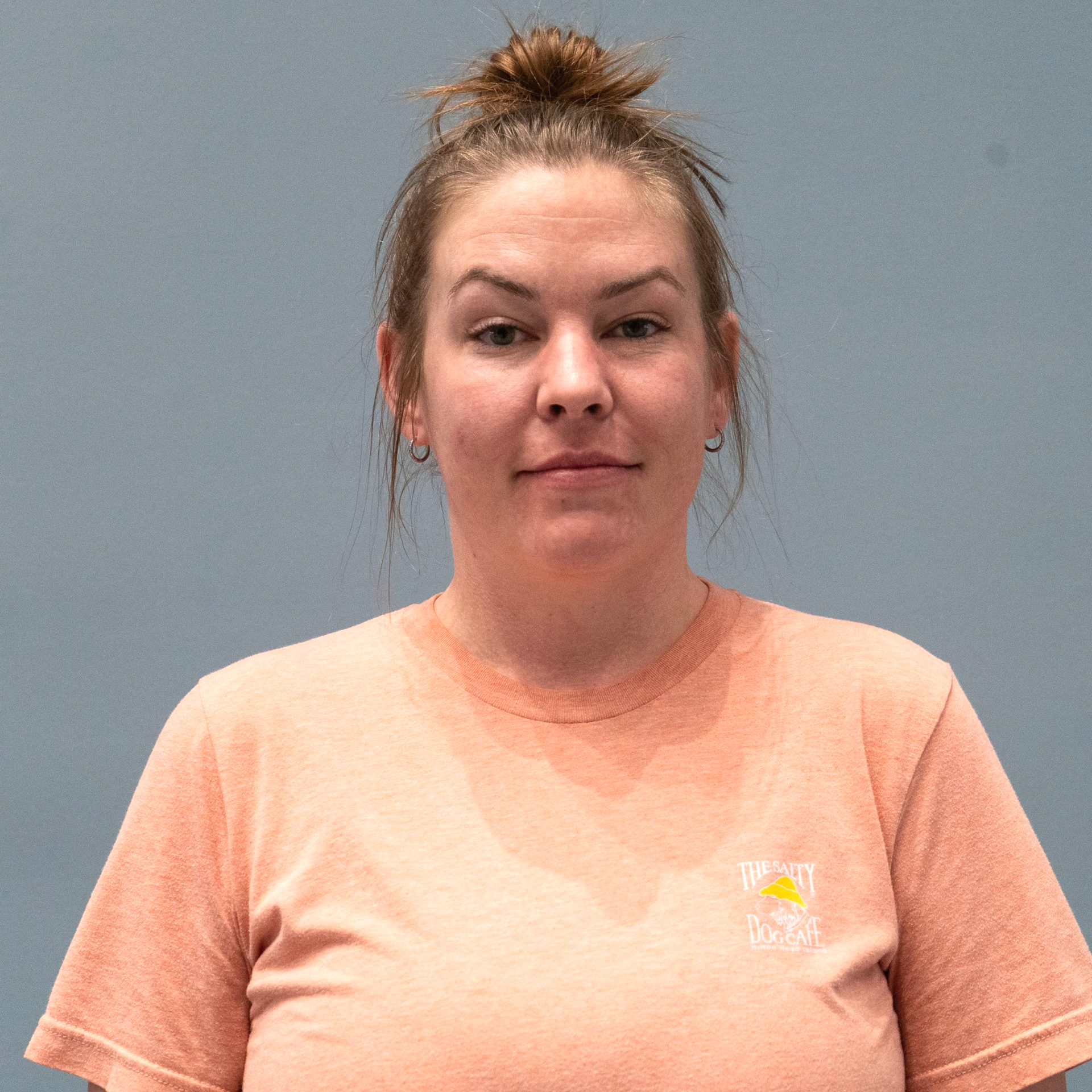 A woman with a bun is wearing a pink shirt, smiling. 