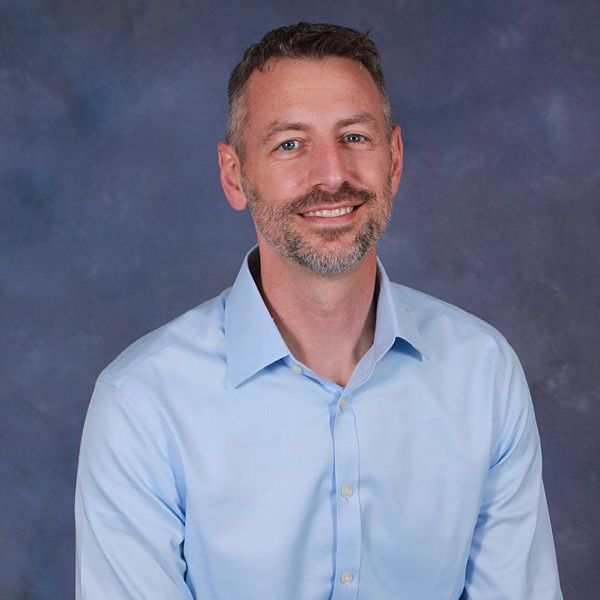 A man with a beard is smiling for the camera while wearing a plaid shirt.