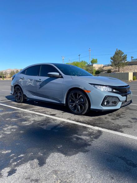 Silver sedan parked in a sunny lot, angled front-left view with blue sky and desert landscaping.
