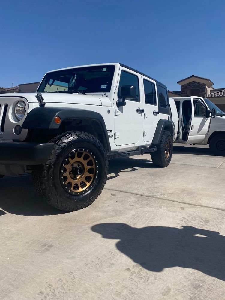 White Jeep Wrangler in a driveway with its rear passenger door open under a clear blue sky