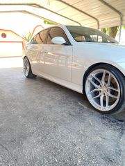 White sedan parked under a covered carport, shown from the front side with shiny alloy wheels.