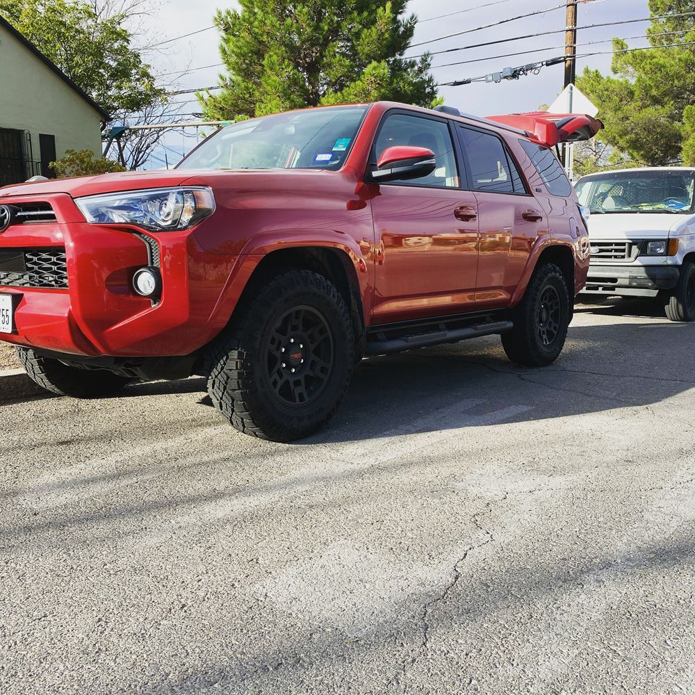 Red SUV parked on a street, with black wheels and a silver truck behind it.