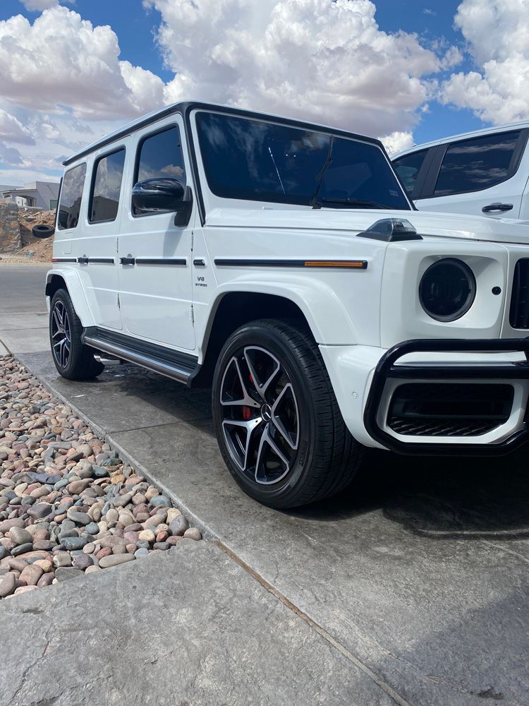 White Mercedes-Benz G-Class SUV parked on a driveway under a cloudy sky.