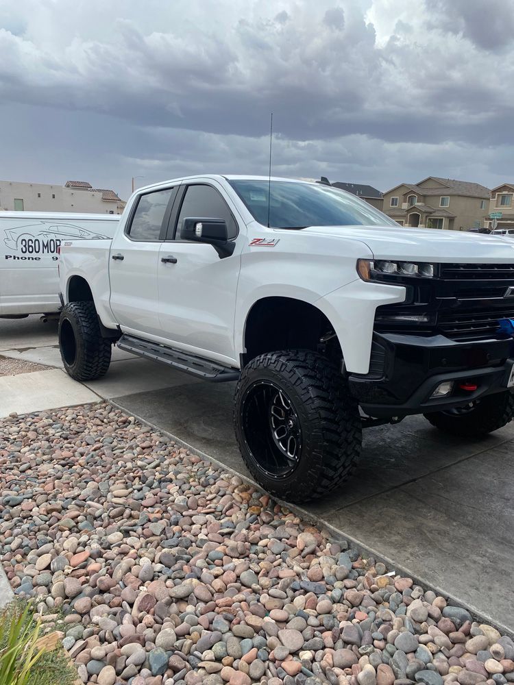 White lifted pickup truck parked on a driveway with gravel landscaping under cloudy skies