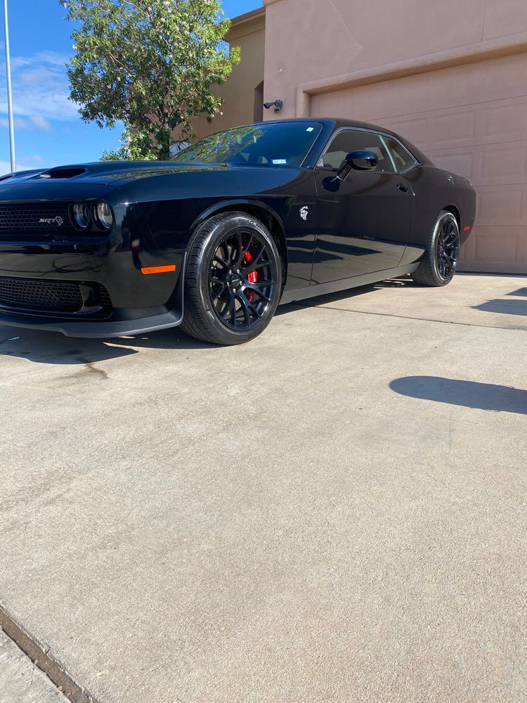 Black Dodge Challenger parked in a sunny lot beside a beige building.