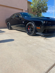 Black Dodge Challenger parked in a sunny lot beside a tan building.