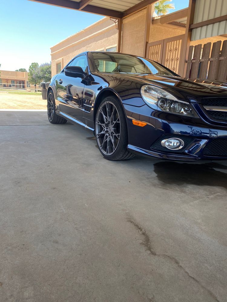 Black sports coupe parked under a wooden carport on a sunny day