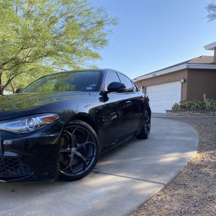 Black sedan parked on a curved driveway beside a garage, with a tree and desert landscaping.