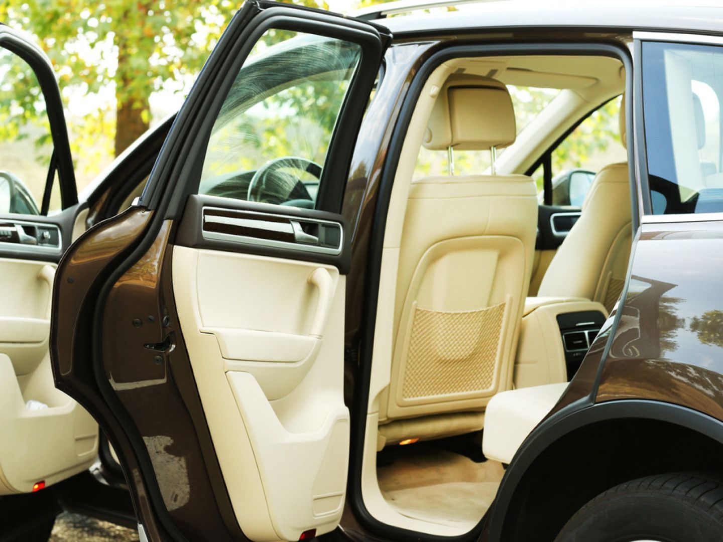 Open car door showing beige leather interior of a dark sedan parked outdoors
