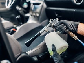Detailing a car interior with a person using a spray gun and holding a cleaning bottle
