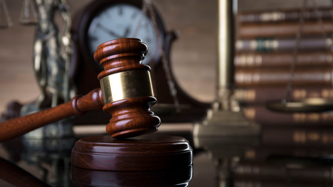 A wooden judge 's gavel is sitting on a table in front of a clock and scales of justice.