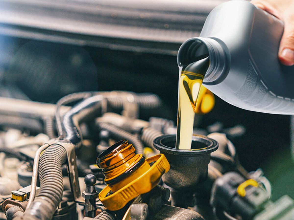 Person pouring motor oil into a car engine; yellow oil, black oil container, engine in focus.