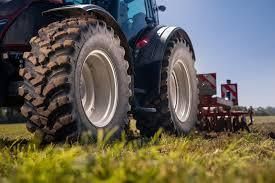 Tractor tilling soil in a field on a sunny day. Large, black tires are visible.