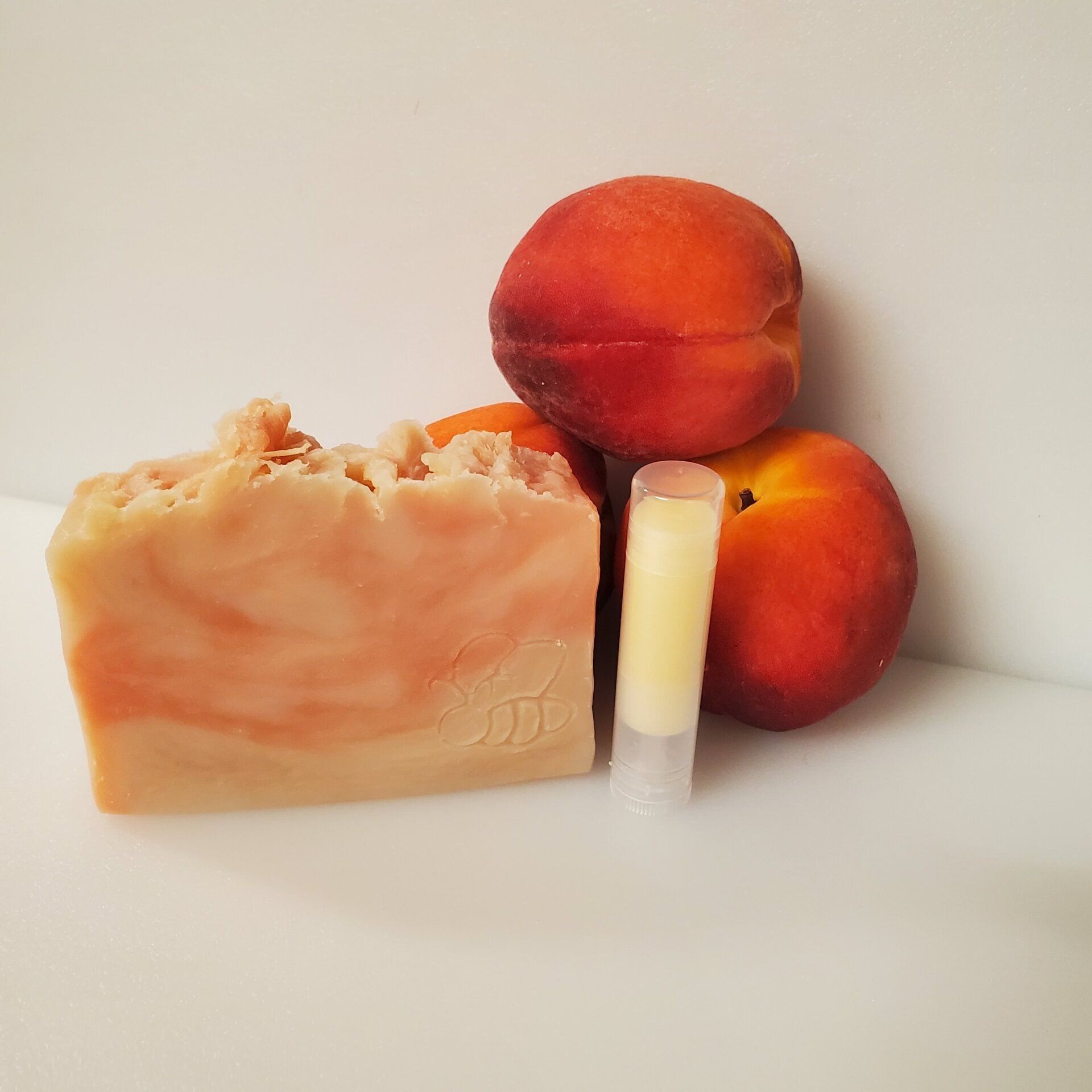 A bar of soap a lip balm and peaches on a table