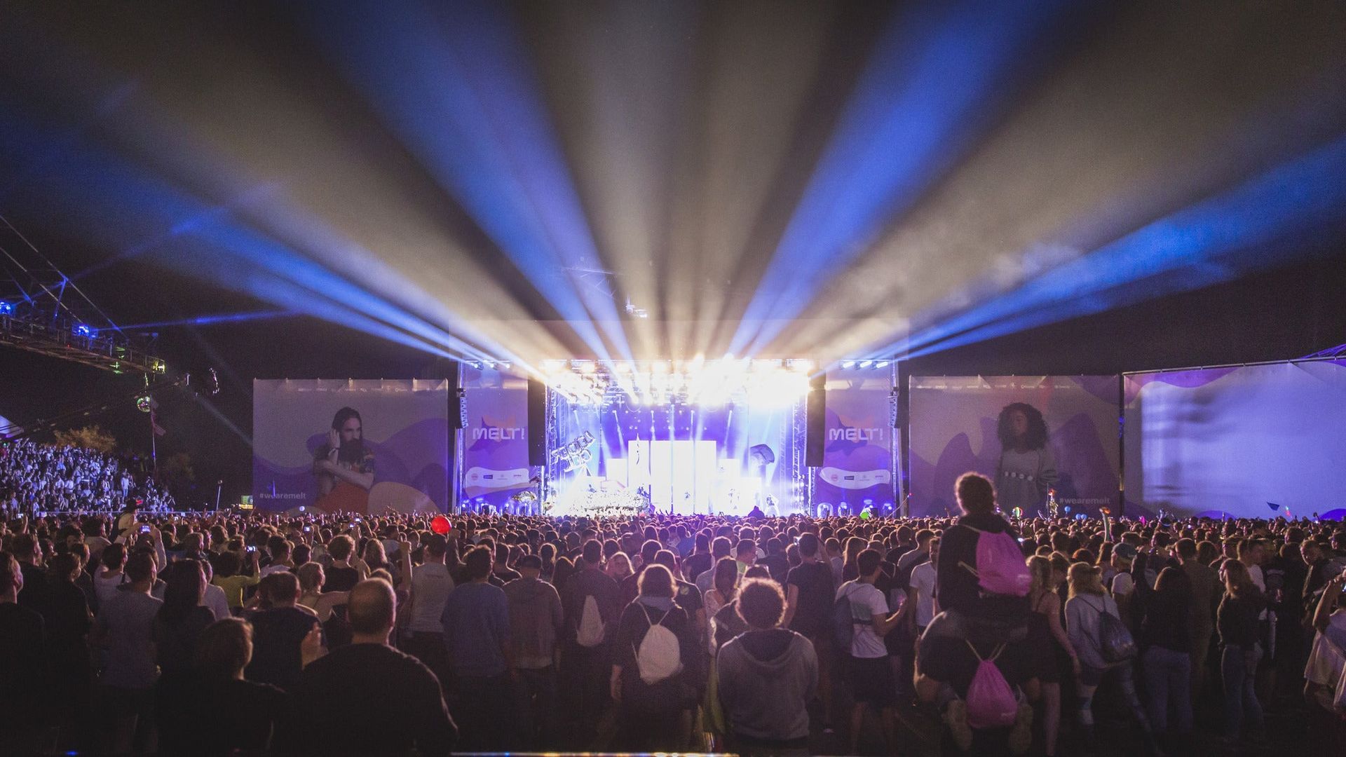 Large outdoor concert with bright lights and a stage, plus thousands of people in a packed crowd