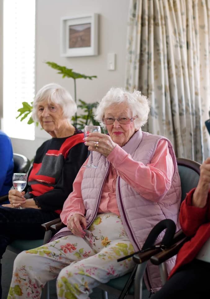 A group of elderly women are sitting in chairs drinking water.