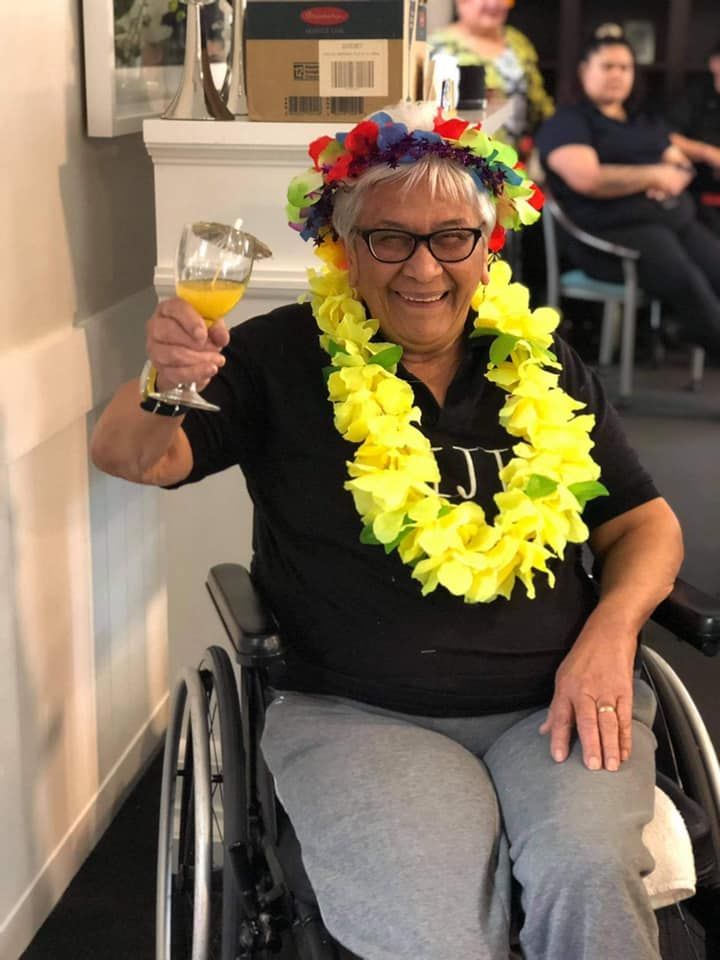 A woman in a wheelchair is wearing a lei and holding a glass of orange juice.