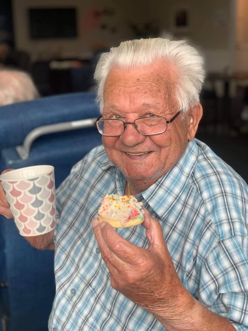 An elderly man is holding a cup of coffee and a donut.