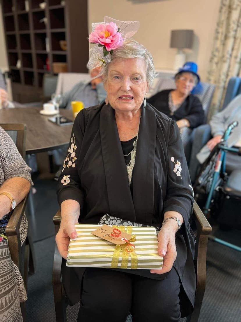An elderly woman is sitting in a chair holding a gift box.