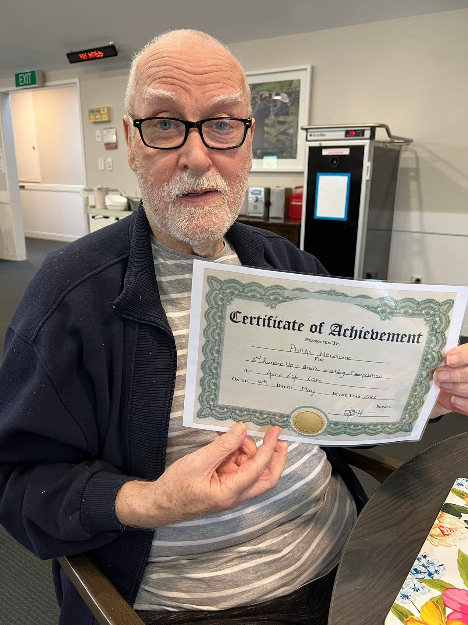 A man with glasses and a beard is holding a certificate of achievement.