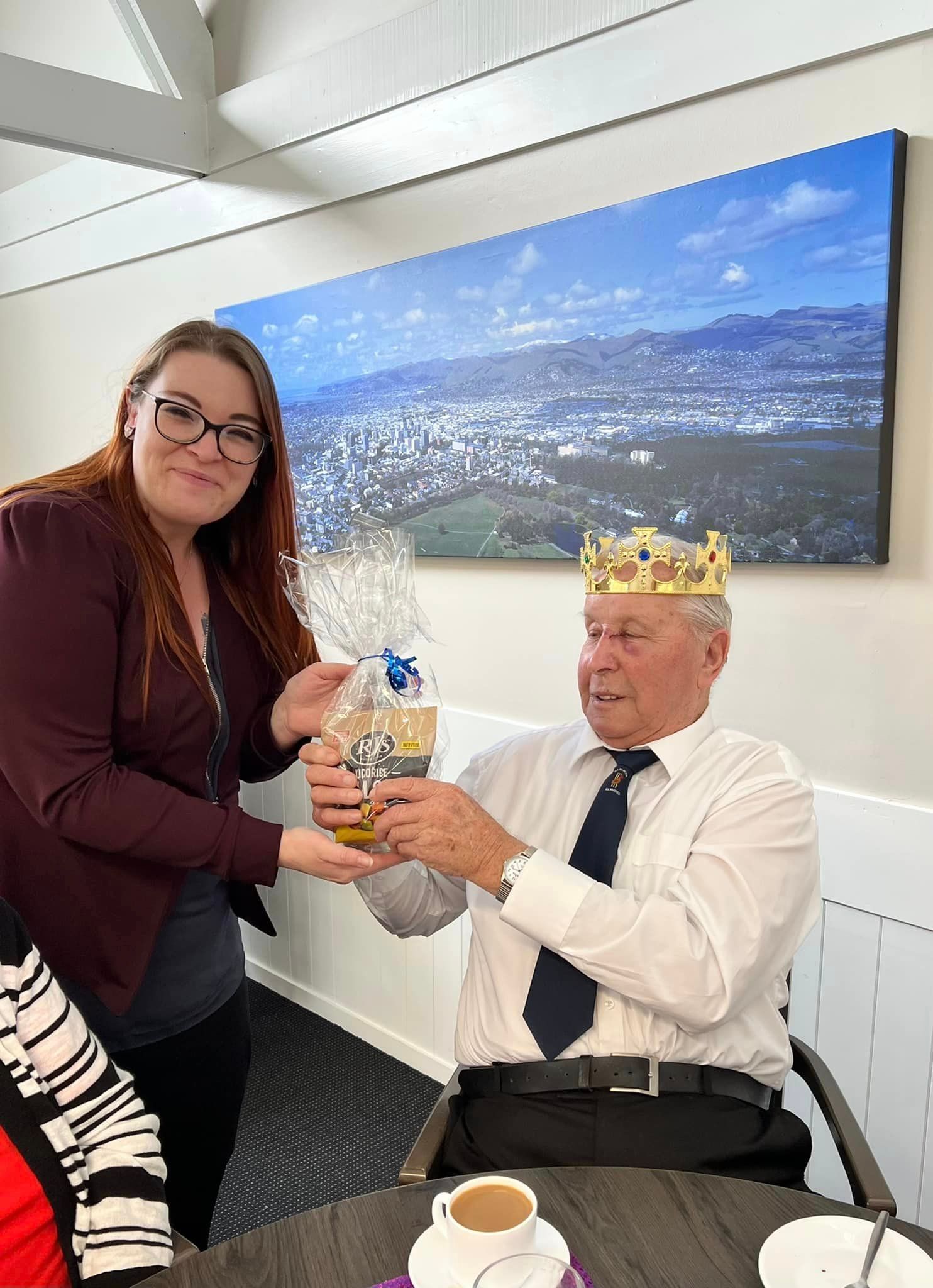 A woman is giving a gift to a man wearing a crown.