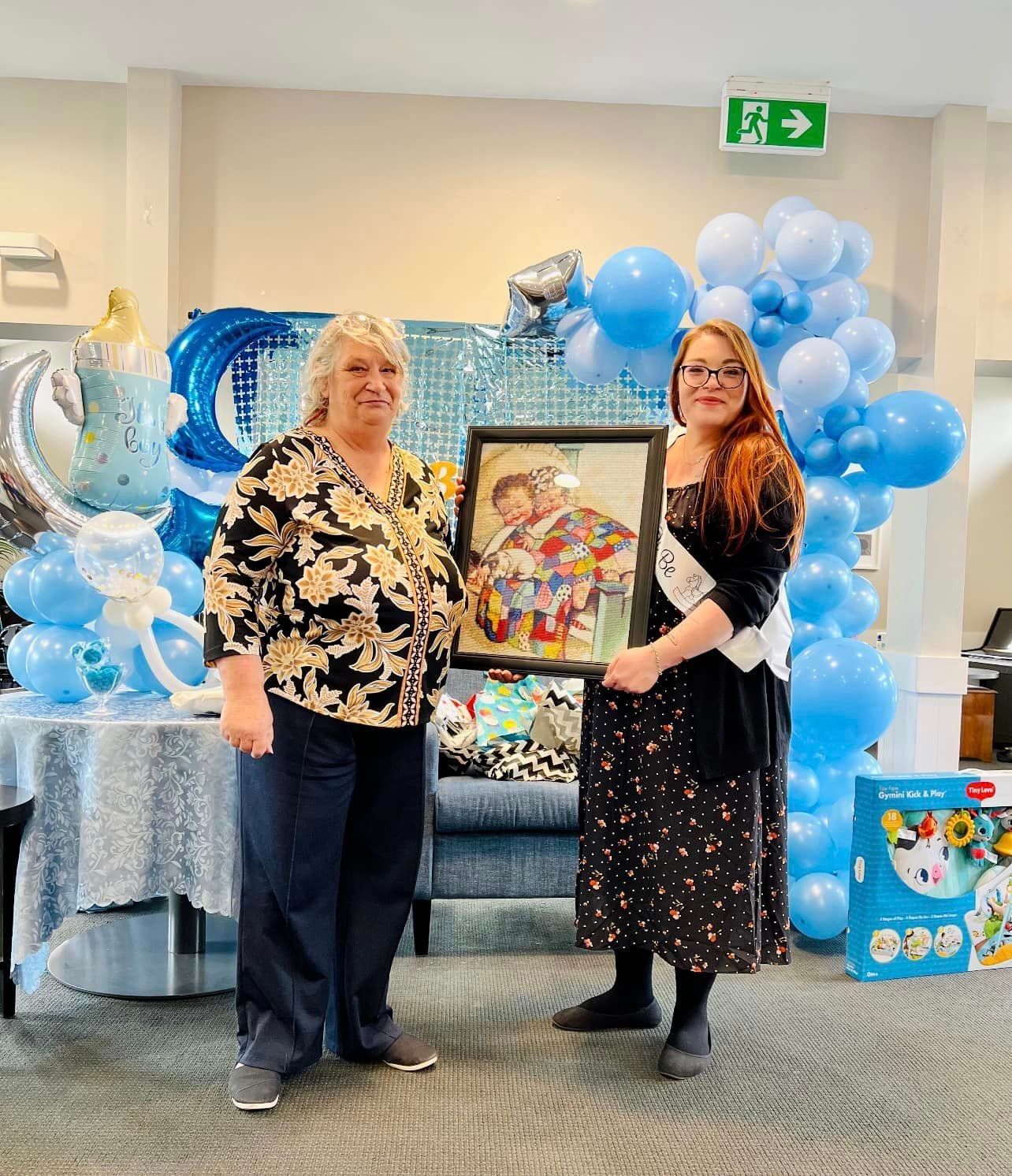 Two women are standing next to each other holding a framed picture.