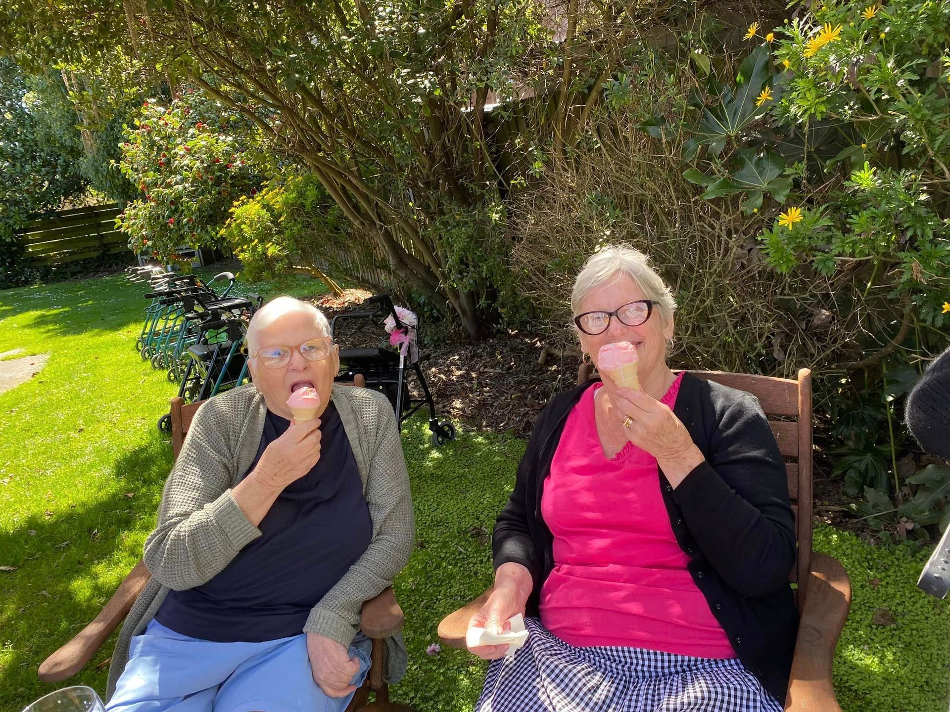 Two older women are sitting in chairs eating ice cream.