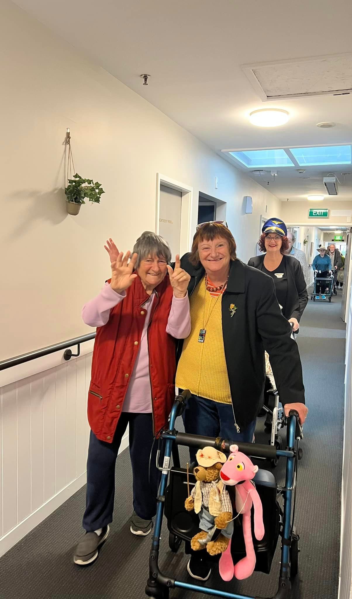 Two women are standing next to each other in a hallway with a walker.