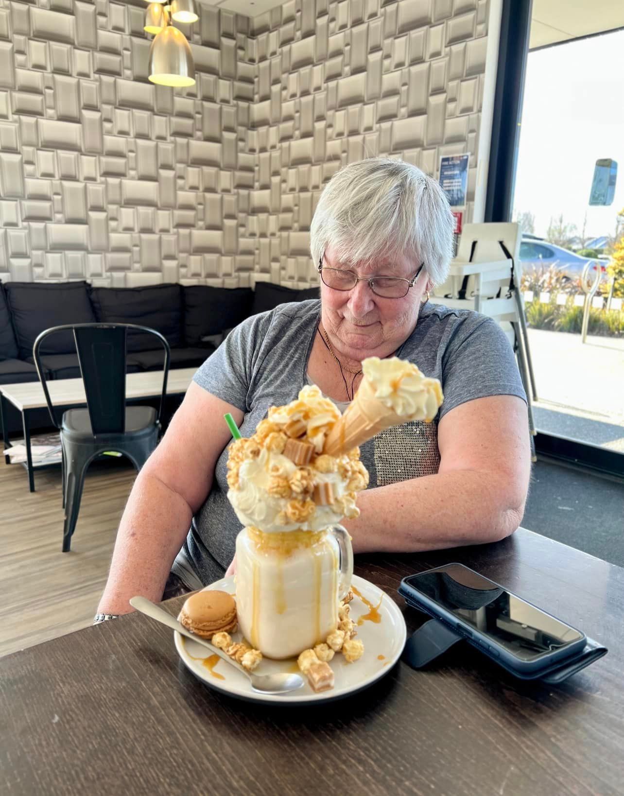 A woman is sitting at a table with a milkshake on it.