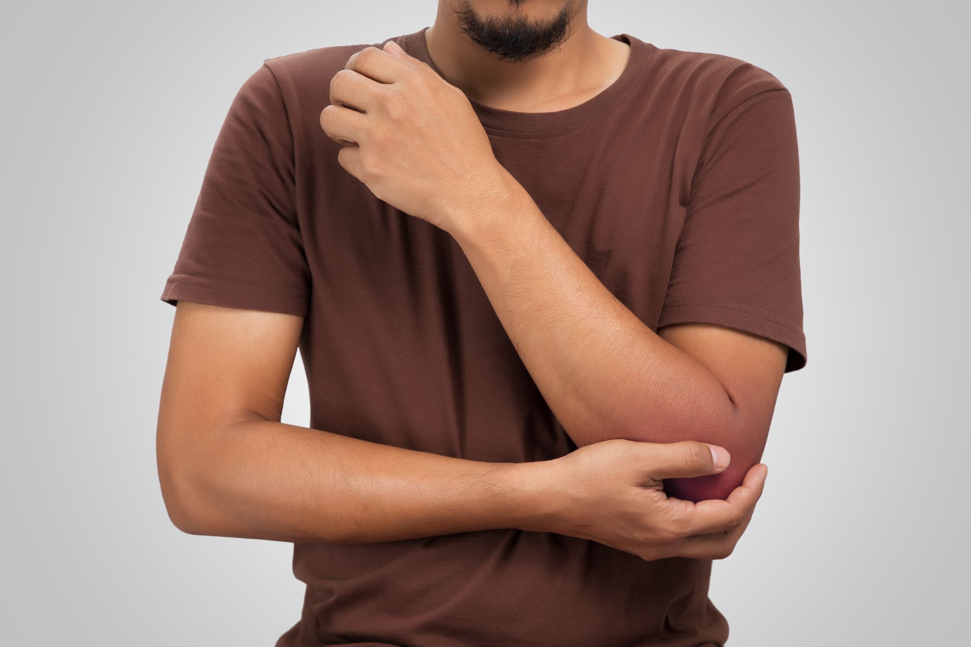 Um homem de camisa marrom está segurando o cotovelo com dor.