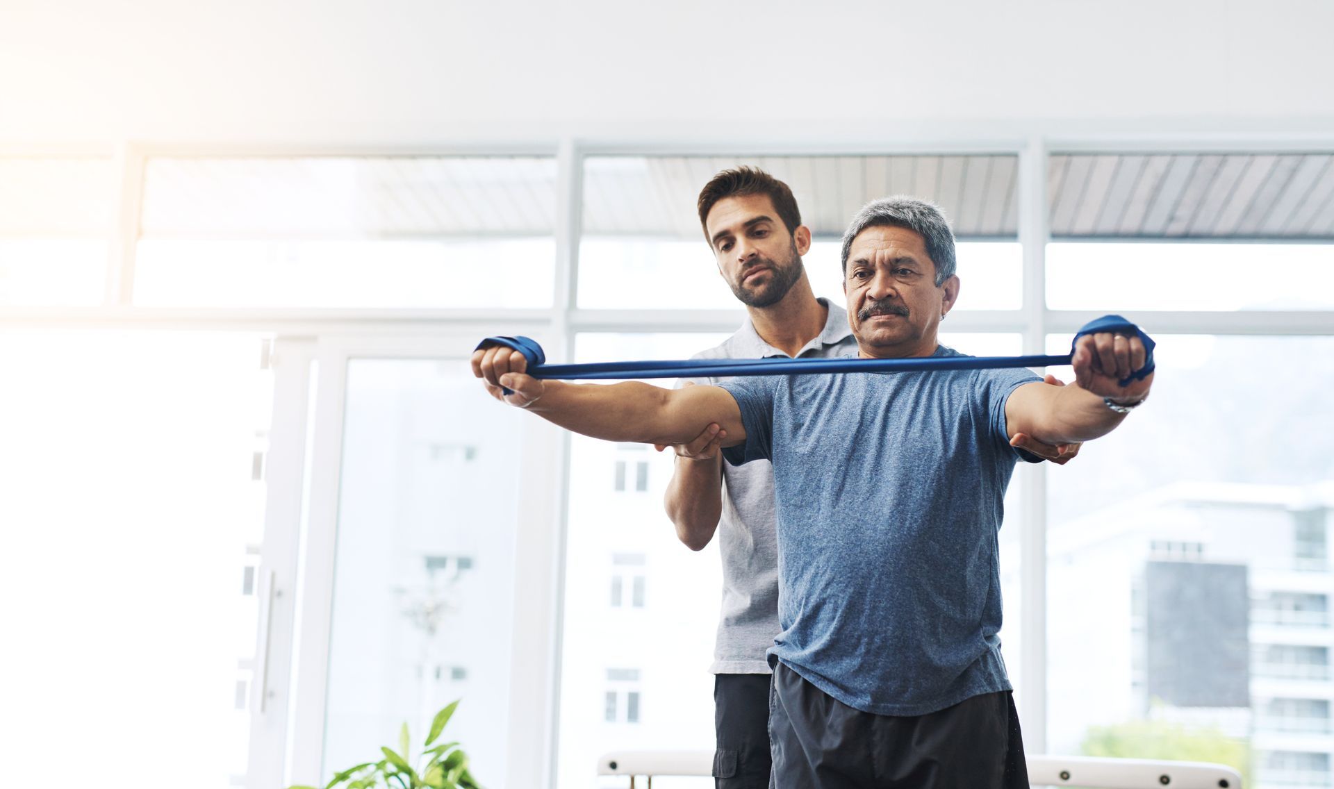 Um homem está sendo ajudado por um personal trainer a esticar os braços com uma faixa de resistência.