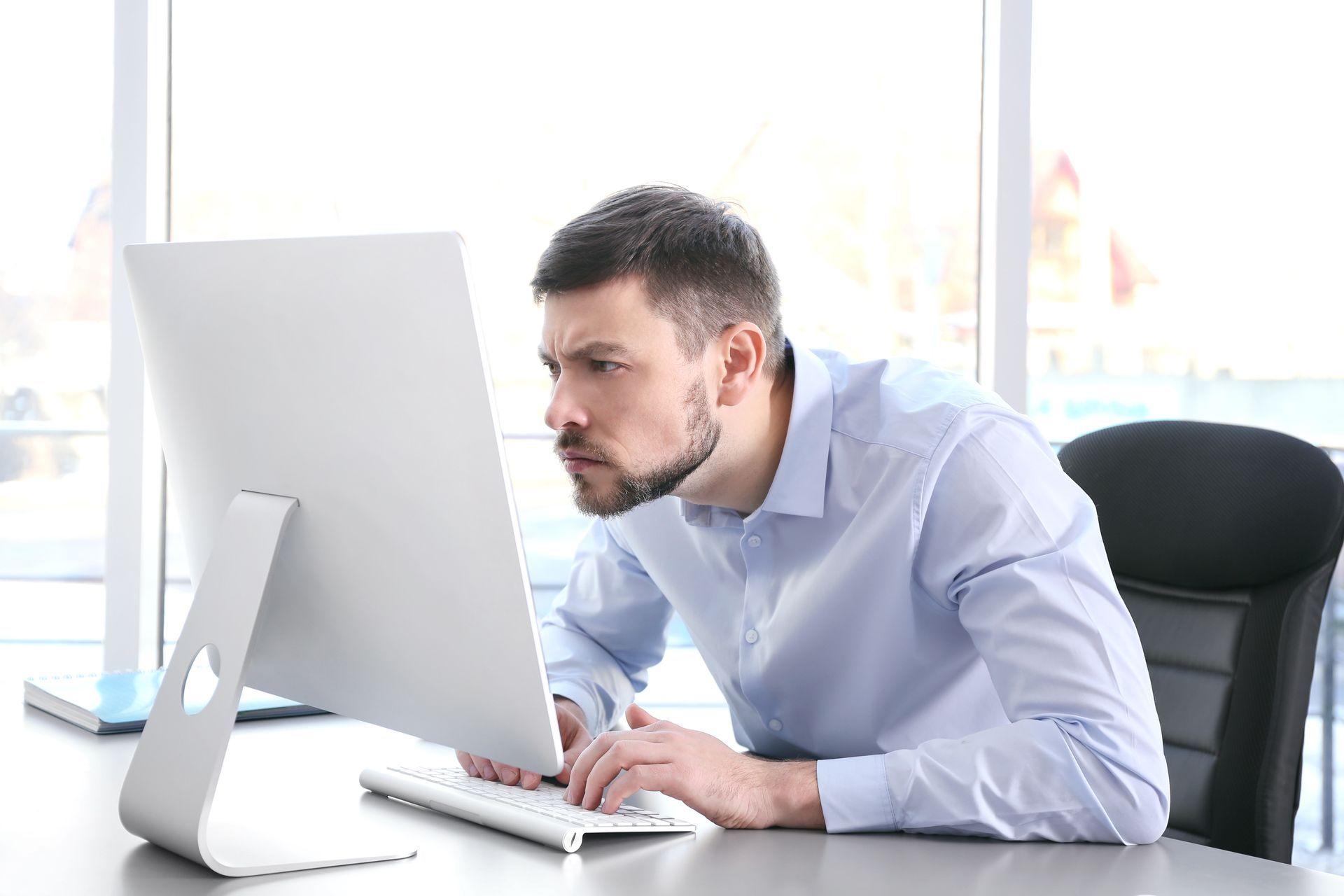 Um homem está sentado em uma mesa olhando para a tela de um computador.
