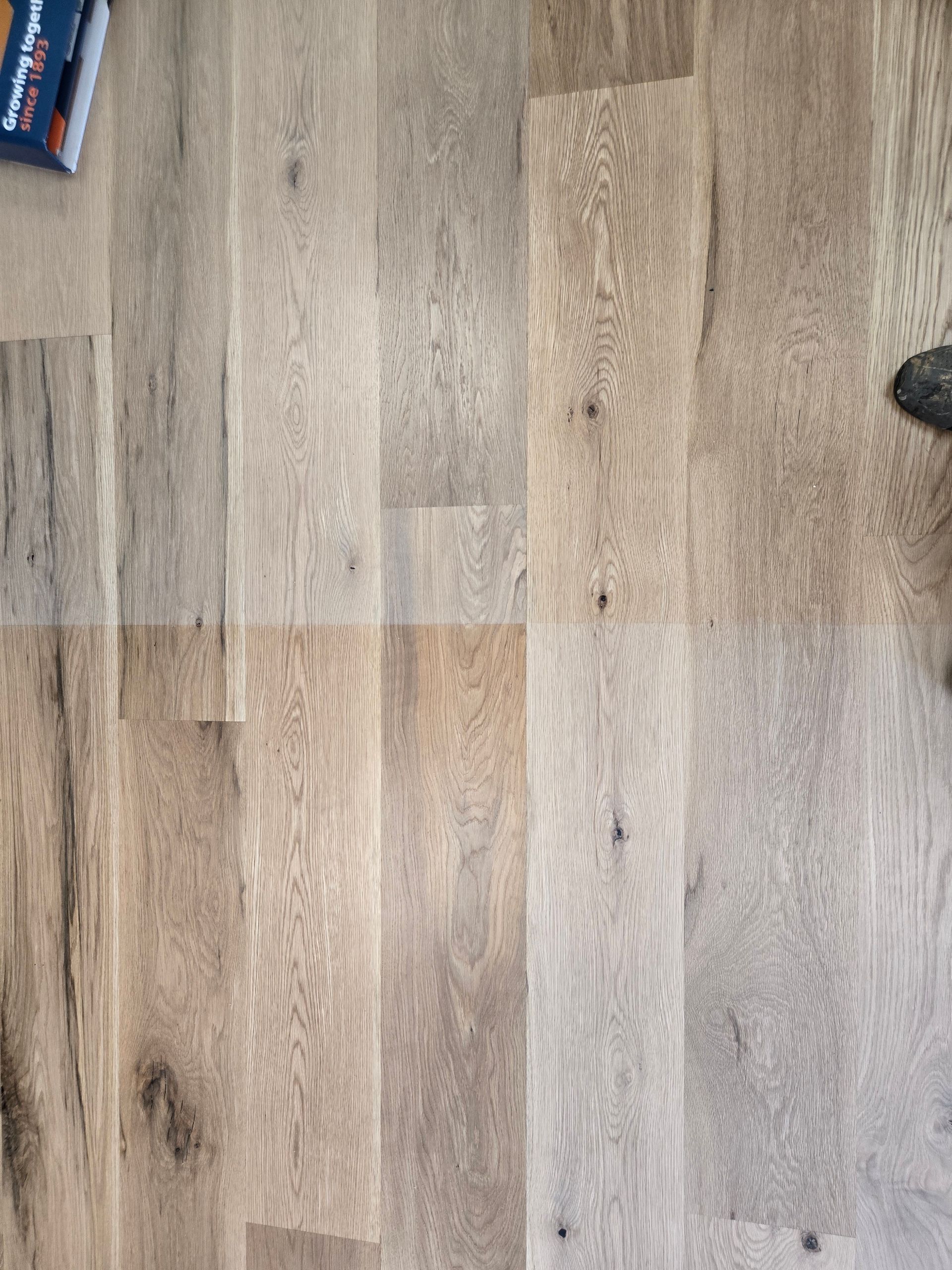 Light wood laminate floor with a blue object in the top-left corner and a dark shoe at the right edge