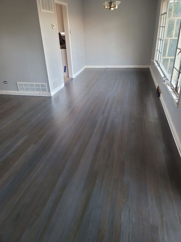 Empty modern living room with gray wood-look floors and large windows along the right wall