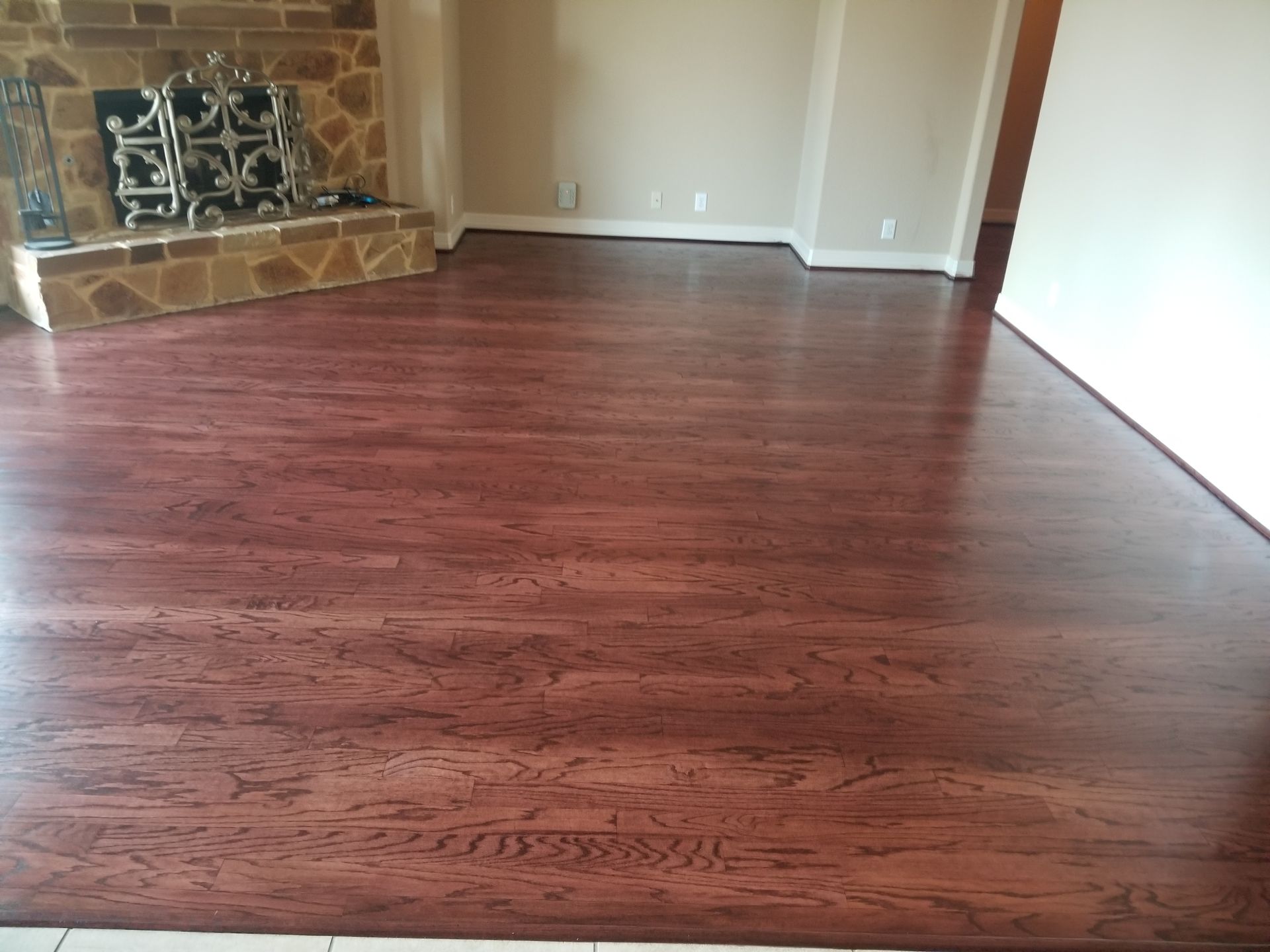 Empty living room with dark wood floor, stone fireplace, and white walls