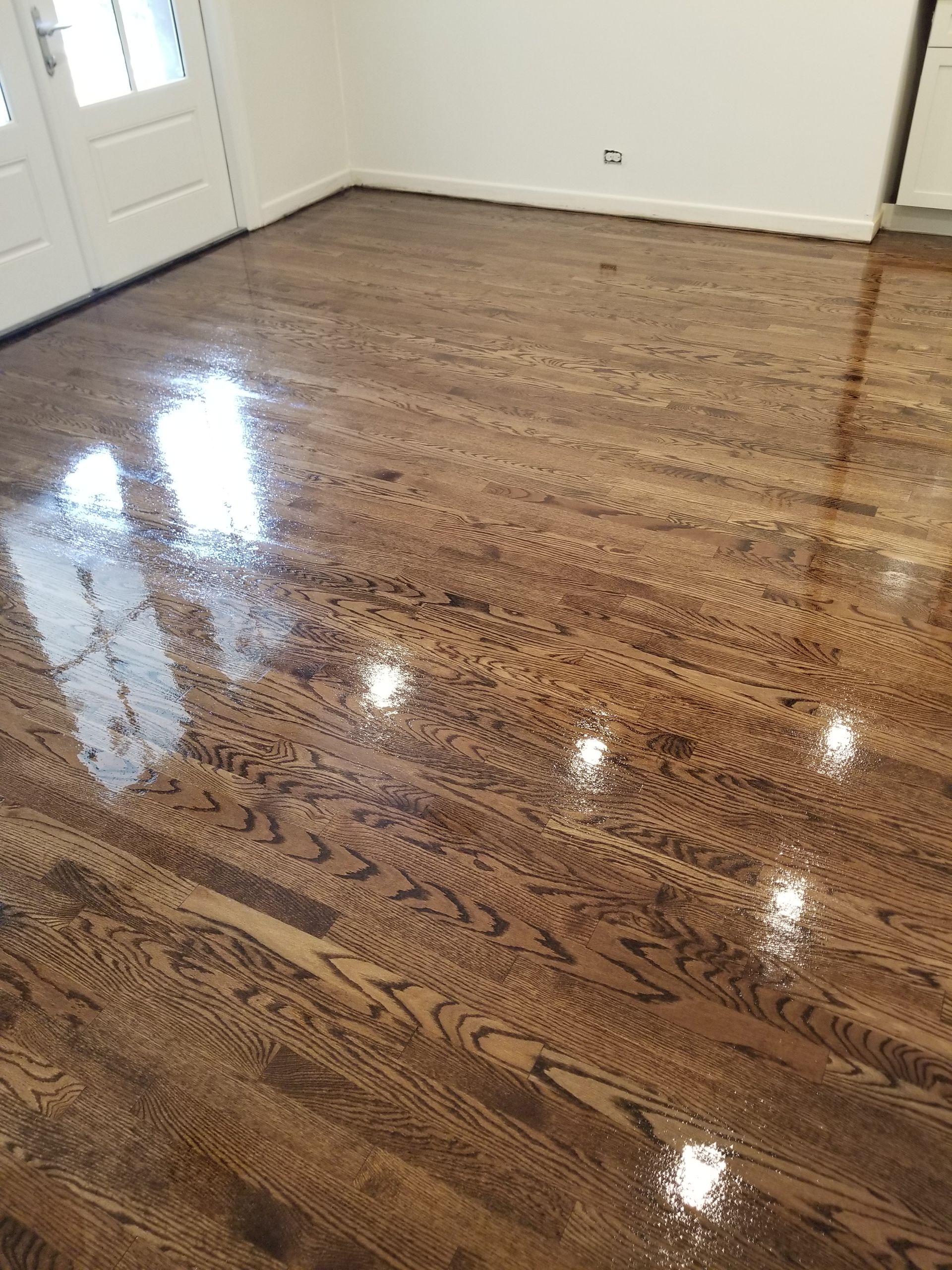 Empty room with glossy hardwood floor and white walls, reflecting light from windows.