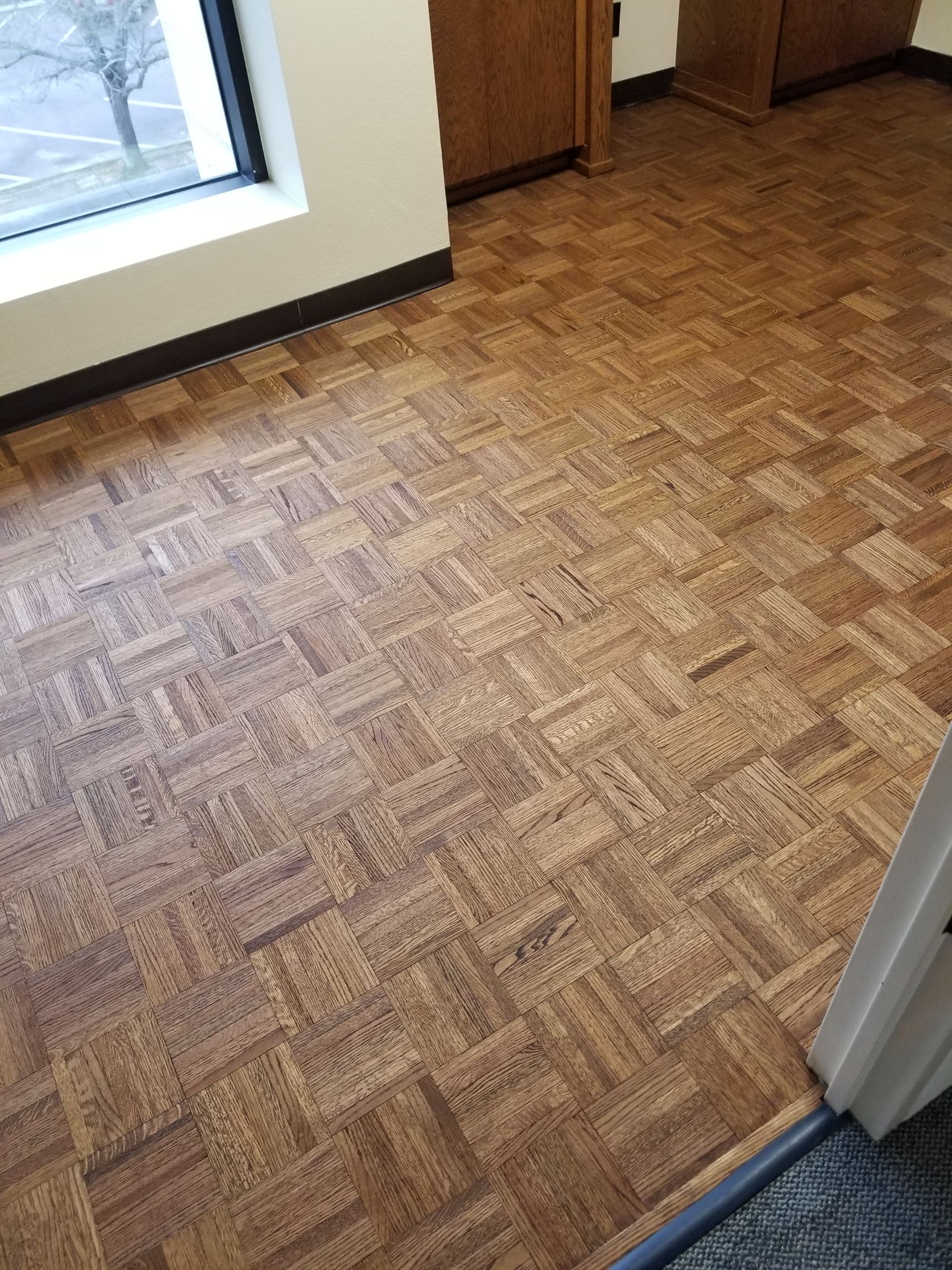 Empty room with patterned wood floor and windows along the wall