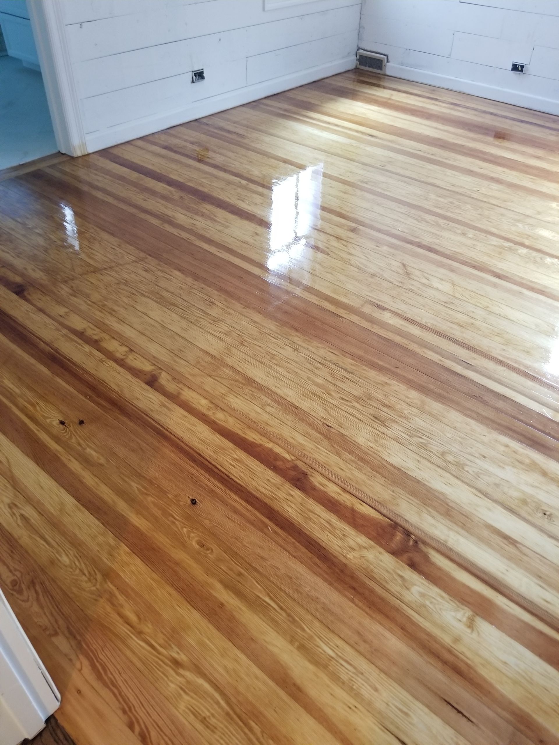 Glossy hardwood floor in a white room with sunlight reflecting off the surface