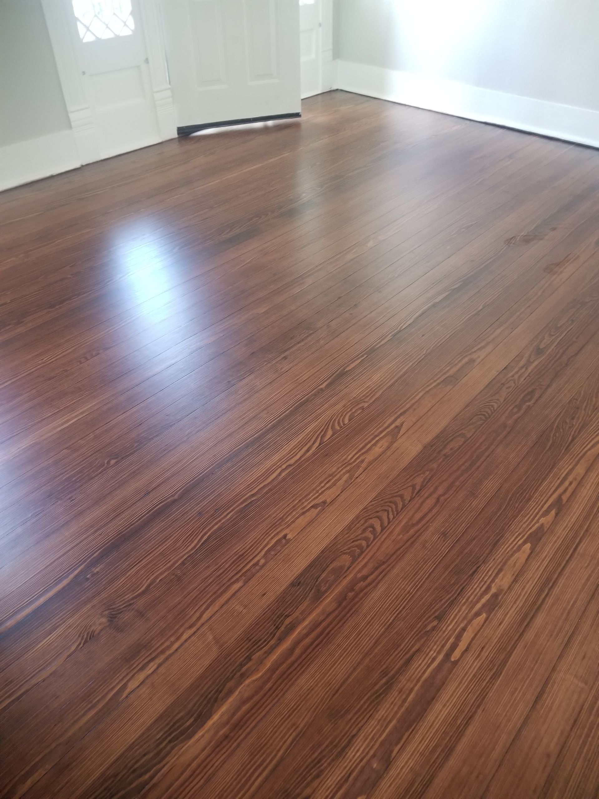 Empty room with glossy dark wood floors and white walls, lit by natural light.